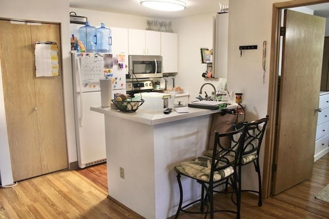 kitchen with white cabinets, light wood-type flooring, appliances with stainless steel finishes, kitchen peninsula, and a breakfast bar