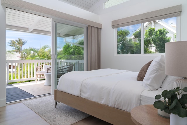 bedroom with vaulted ceiling, wood finished floors, and access to outside