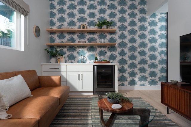 living room featuring wallpapered walls, an accent wall, beverage cooler, a dry bar, and wood finished floors