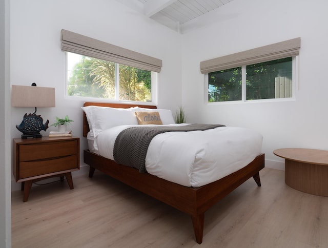 bedroom featuring beam ceiling, light wood-style flooring, and baseboards