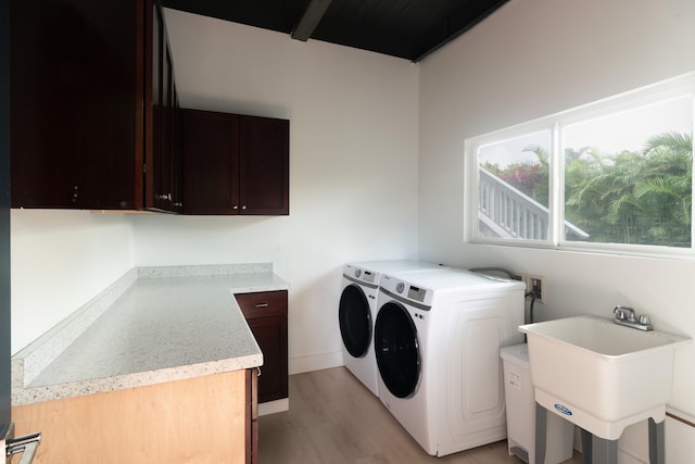 clothes washing area with baseboards, cabinet space, a sink, washer and dryer, and light wood-type flooring