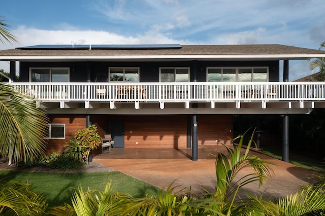 view of front of home featuring solar panels, a patio area, and roof with shingles