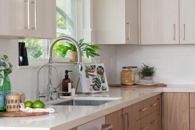 kitchen with backsplash, modern cabinets, light countertops, and a sink