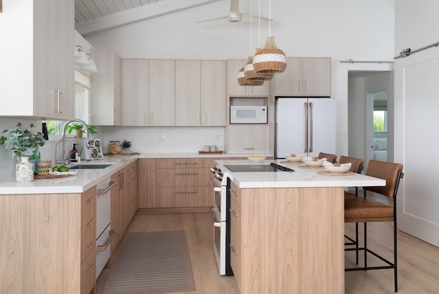 kitchen featuring light brown cabinetry, a sink, white appliances, a breakfast bar area, and vaulted ceiling with beams