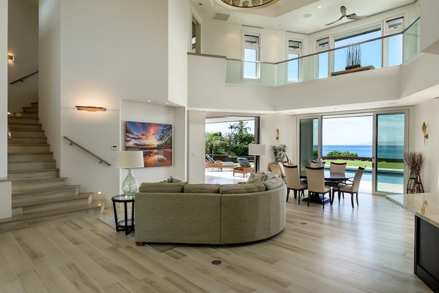 living room featuring a high ceiling, a water view, ceiling fan, and light hardwood / wood-style flooring