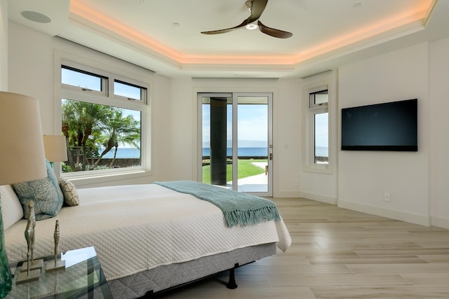 bedroom with multiple windows, a water view, and a raised ceiling