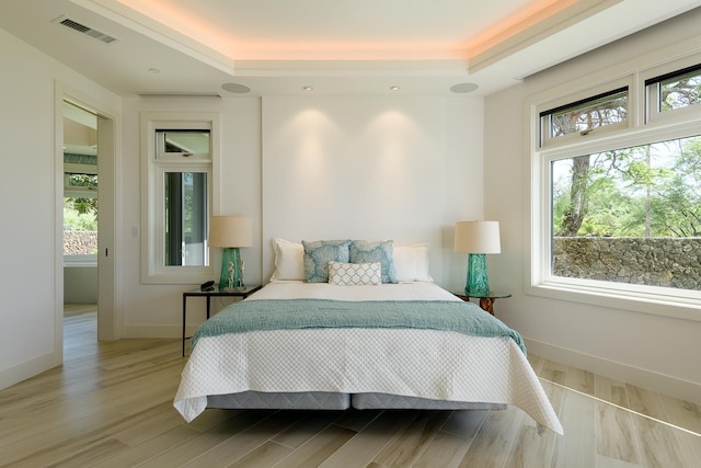 bedroom featuring hardwood / wood-style floors, a tray ceiling, and multiple windows