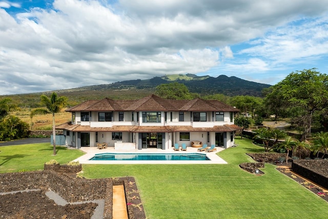 rear view of property featuring a mountain view, a patio, and a lawn