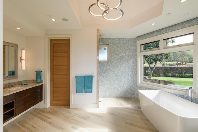 bathroom featuring a notable chandelier, vanity, hardwood / wood-style flooring, and a tub