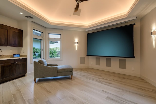 cinema featuring light hardwood / wood-style floors, ceiling fan, and a tray ceiling