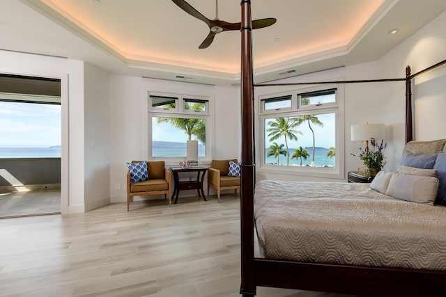 bedroom featuring a water view, light hardwood / wood-style floors, ceiling fan, and a tray ceiling