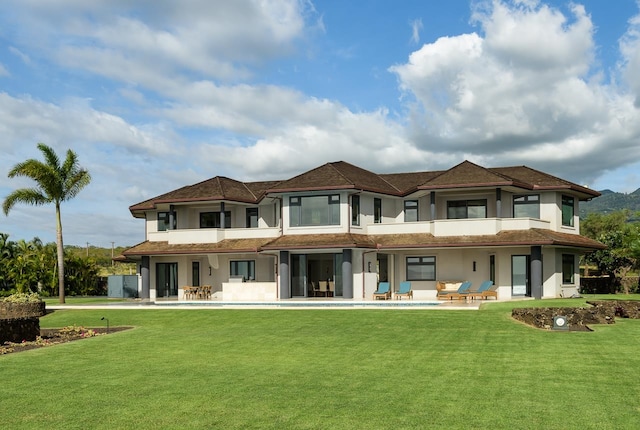 rear view of house with a patio area, a balcony, and a lawn