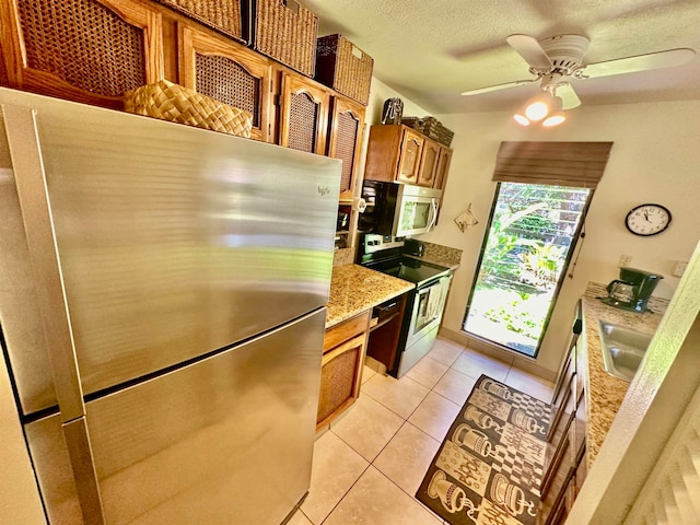 kitchen featuring light tile floors, ceiling fan, appliances with stainless steel finishes, light stone counters, and sink