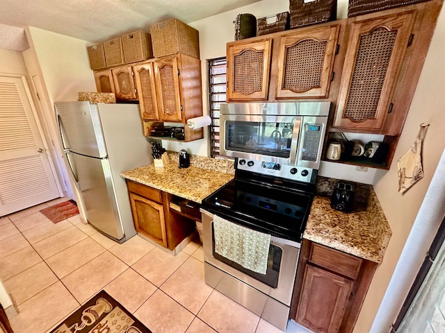 kitchen with stainless steel appliances, light tile floors, and light stone countertops