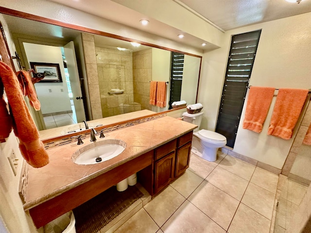 bathroom featuring oversized vanity, tile flooring, toilet, and tiled shower