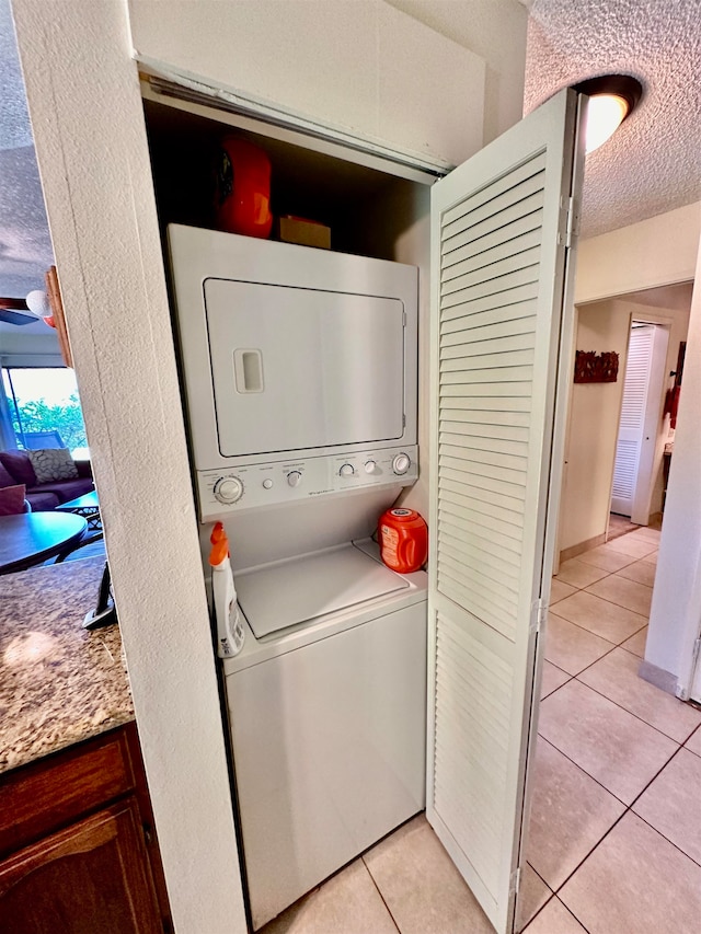 clothes washing area featuring stacked washing maching and dryer, a textured ceiling, and light tile floors