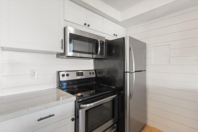 2737 S Kihei Rd Unit 160, Kihei, HI 96753 - kitchen featuring appliances with stainless steel finishes, white cabinetry, light stone counters, and wood walls