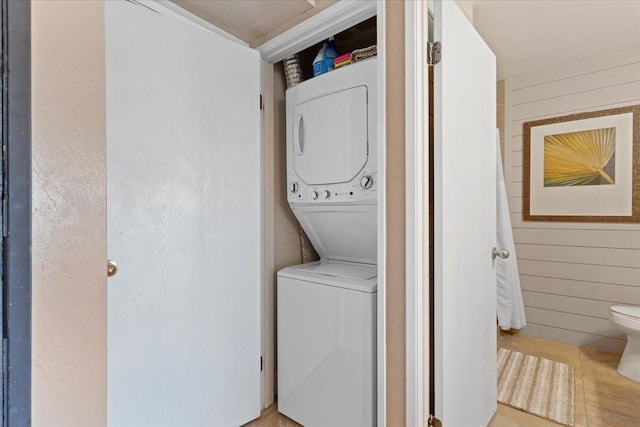 laundry area with wood walls, light tile patterned floors, and stacked washer and clothes dryer