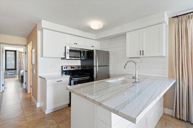 kitchen with kitchen peninsula, appliances with stainless steel finishes, light stone counters, sink, and white cabinetry