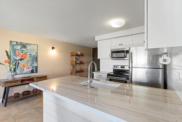 kitchen featuring sink, light stone countertops, light tile patterned floors, white cabinetry, and stainless steel appliances