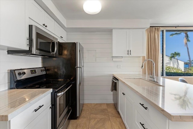 kitchen with wood walls, sink, light stone counters, white cabinetry, and stainless steel appliances