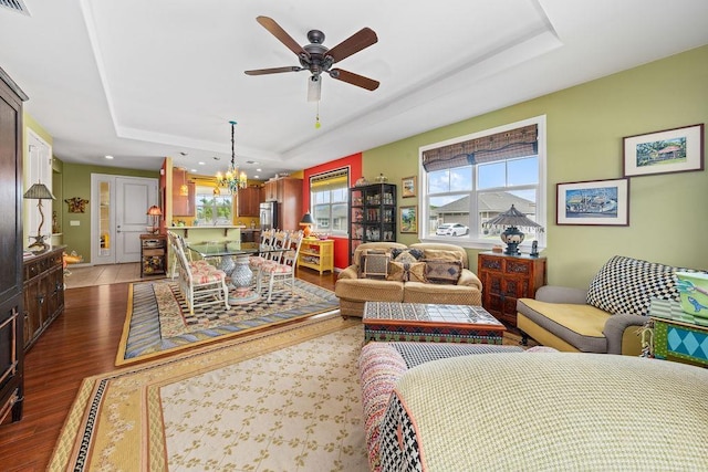 living room featuring a raised ceiling, dark wood-type flooring, and ceiling fan with notable chandelier