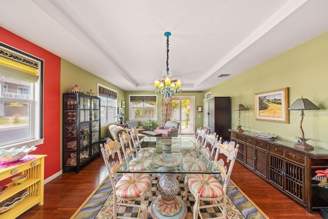 dining space with a raised ceiling, dark hardwood / wood-style floors, and a chandelier