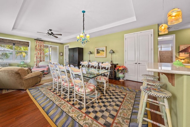 dining area with a raised ceiling, dark hardwood / wood-style flooring, and ceiling fan with notable chandelier