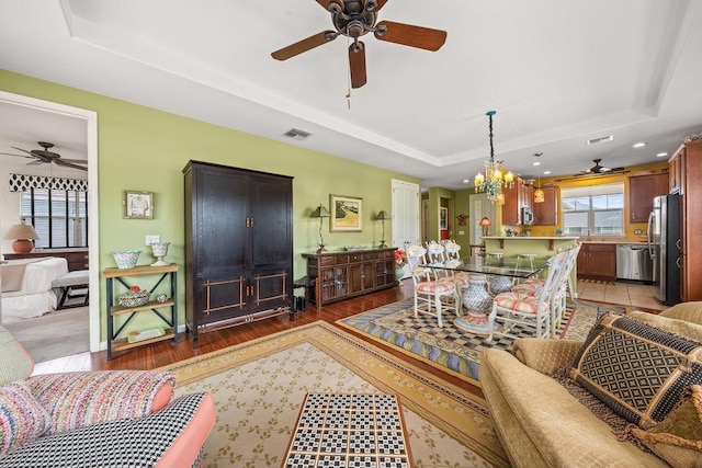 living room with dark hardwood / wood-style flooring, ceiling fan with notable chandelier, and a tray ceiling