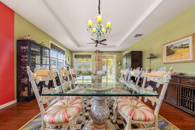 dining room featuring ceiling fan with notable chandelier, a tray ceiling, and dark hardwood / wood-style flooring