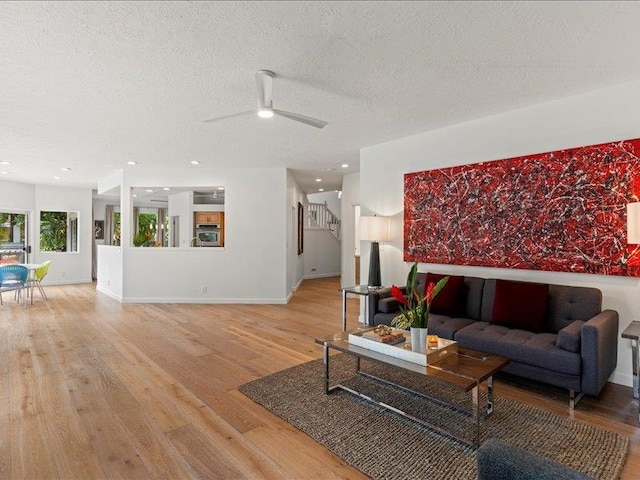 living room with light wood-type flooring, ceiling fan, and a textured ceiling