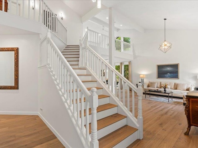 stairway featuring hardwood / wood-style floors, beam ceiling, and a towering ceiling