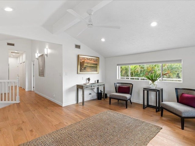 living area featuring a textured ceiling, light wood-type flooring, lofted ceiling with beams, and ceiling fan