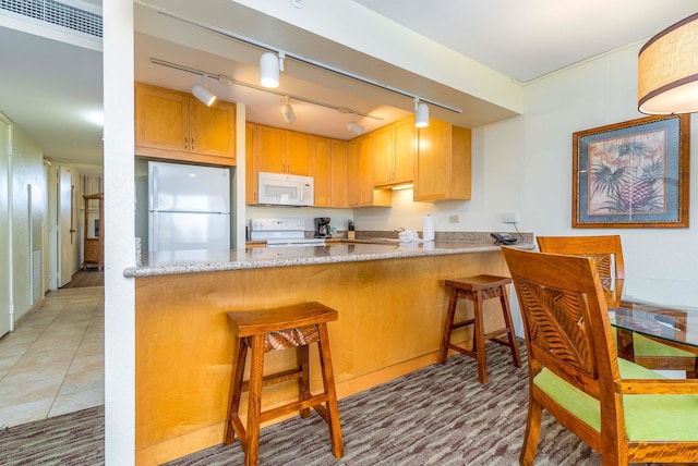 kitchen with kitchen peninsula, white appliances, rail lighting, light stone countertops, and a kitchen bar