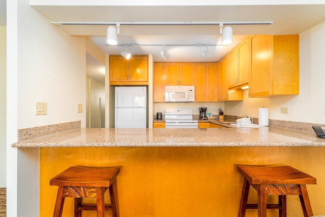 kitchen featuring white appliances, a kitchen bar, rail lighting, and kitchen peninsula