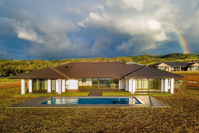 rear view of property with stucco siding, a standing seam roof, a patio area, metal roof, and an outdoor pool