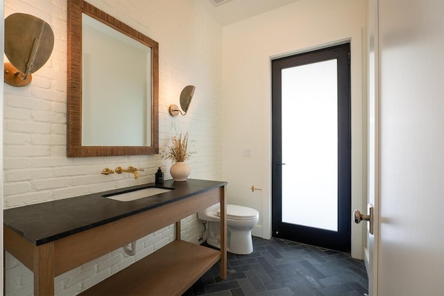 bathroom featuring brick wall, a sink, and toilet