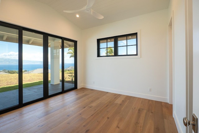 unfurnished room with ceiling fan, hardwood / wood-style flooring, a water view, baseboards, and vaulted ceiling