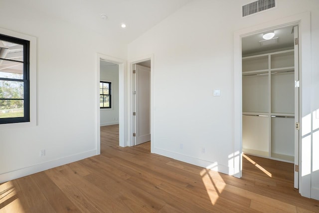 unfurnished bedroom with lofted ceiling, visible vents, a spacious closet, wood finished floors, and baseboards