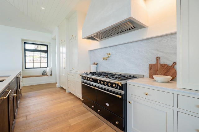 kitchen featuring premium range hood, light wood-style floors, white cabinetry, and double oven range