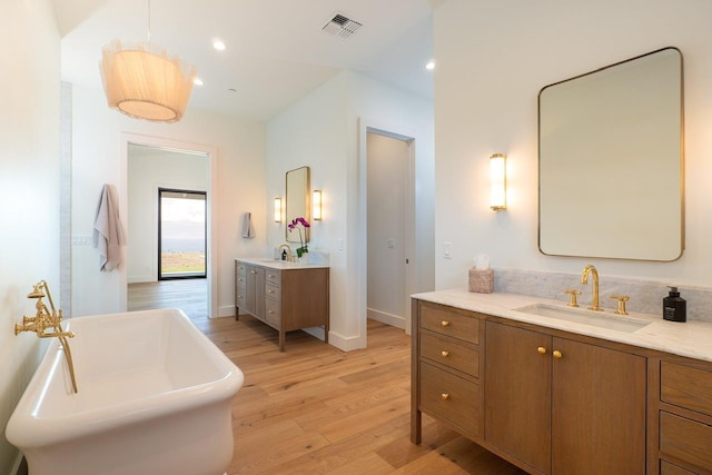 full bath with visible vents, a soaking tub, wood finished floors, a sink, and two vanities