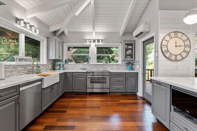 kitchen with light stone countertops, lofted ceiling with beams, an AC wall unit, gray cabinets, and appliances with stainless steel finishes