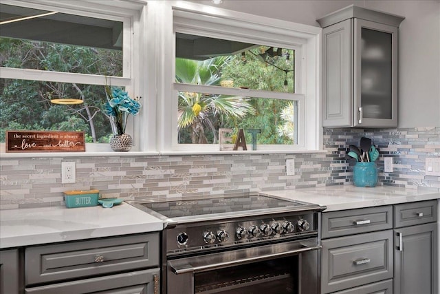 kitchen featuring decorative backsplash, gray cabinets, light stone counters, and stainless steel stove