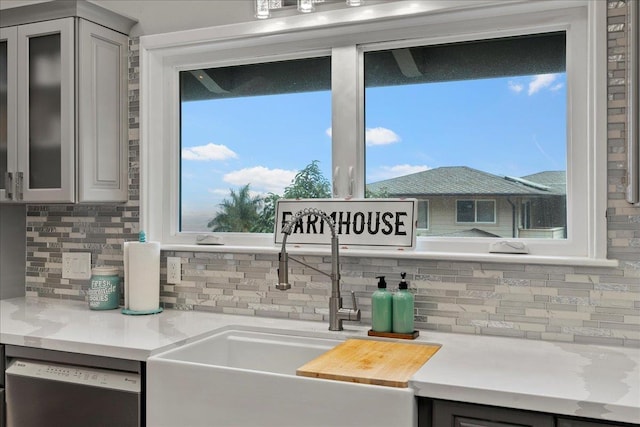 kitchen with stainless steel dishwasher, plenty of natural light, gray cabinets, and backsplash