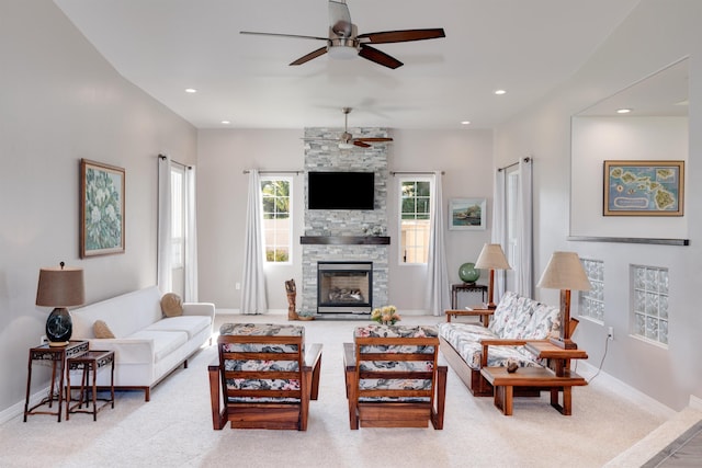 living room with a stone fireplace, light colored carpet, and ceiling fan