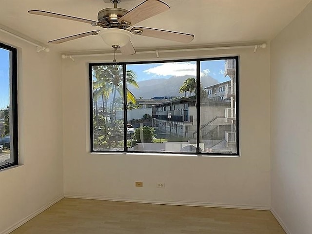 unfurnished room with ceiling fan, a mountain view, and light hardwood / wood-style floors