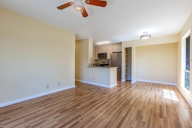 unfurnished living room featuring a ceiling fan, light wood finished floors, baseboards, and a sink