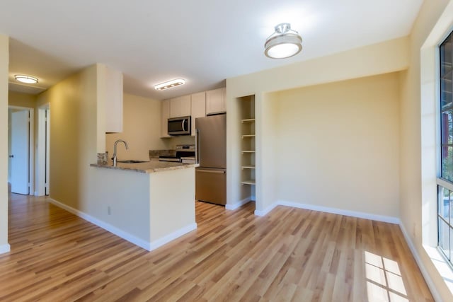 kitchen with light wood finished floors, a sink, appliances with stainless steel finishes, and white cabinetry