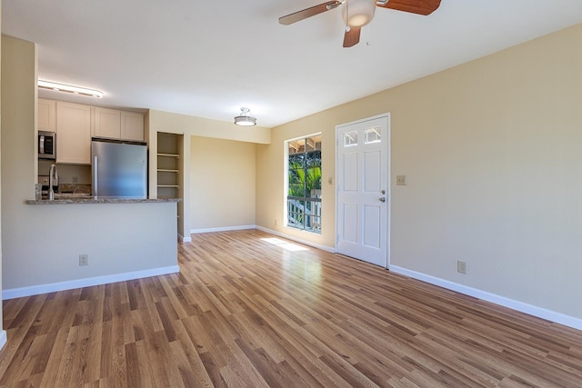 unfurnished living room featuring sink, built in shelves, light wood-type flooring, and ceiling fan