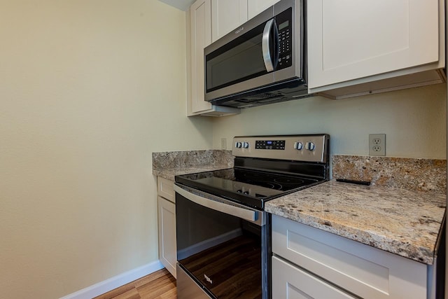 kitchen featuring light stone countertops, appliances with stainless steel finishes, light wood-type flooring, and white cabinets